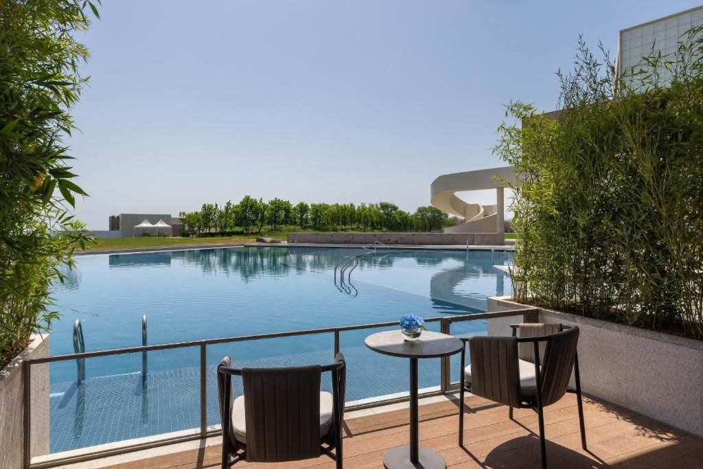 A swimming pool with a glass barrier, surrounded by outdoor seating and greenery.