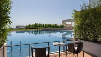 A swimming pool with a glass barrier, surrounded by outdoor seating and greenery.