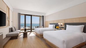Quarto de hotel com duas camas, um sofá, uma TV e uma varanda com vista para o mar.
