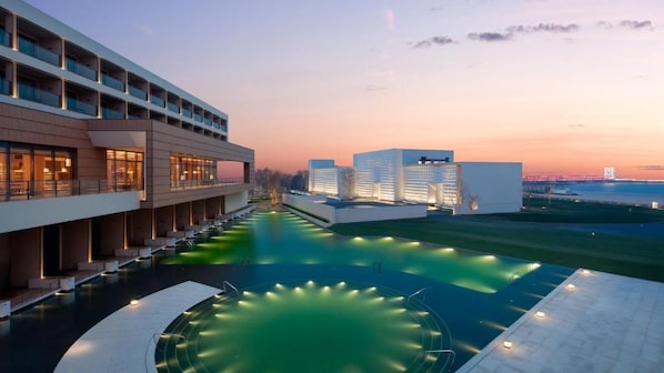 A modern hotel with a swimming pool, multiple floors, and a view of a bridge in the background.