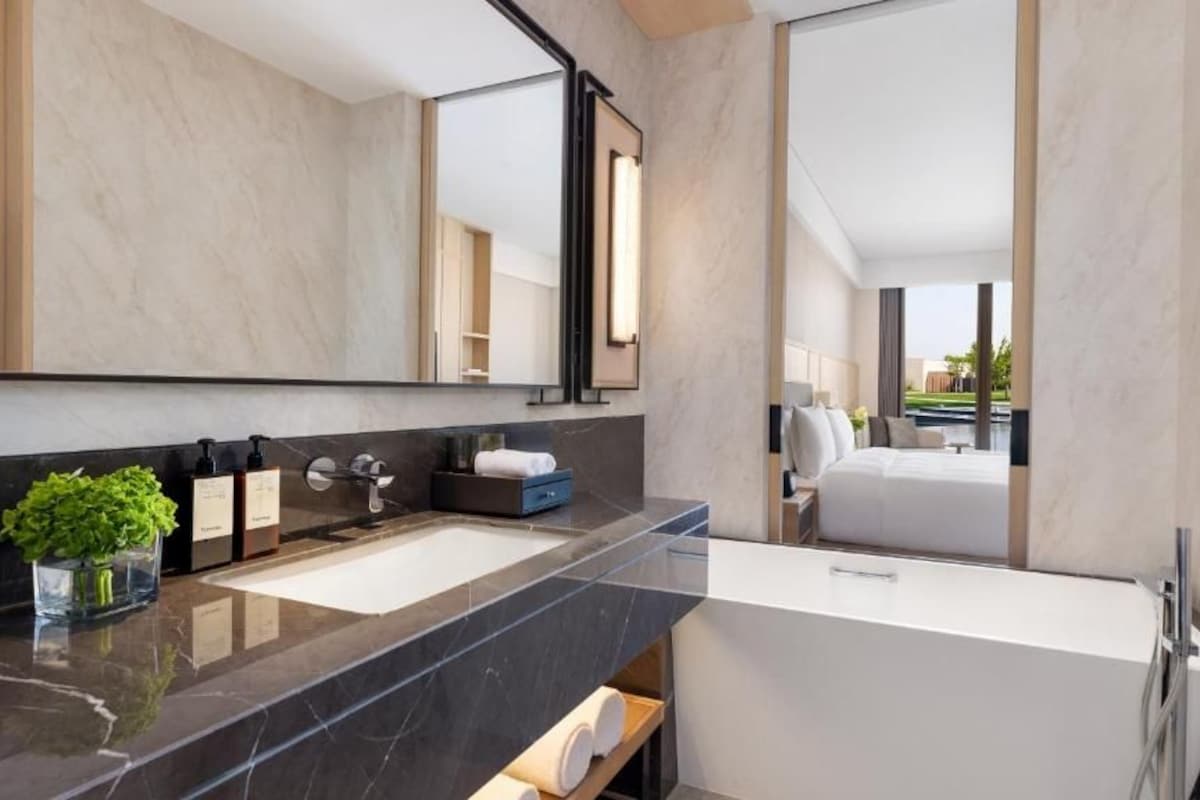 A modern bathroom with a large mirror, two sinks, a bathtub, and a potted plant.
