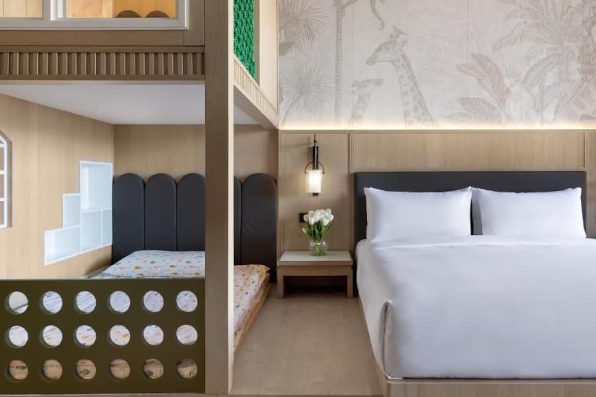 A hotel room with a bed, bedside tables, a nightstand, a wall with a giraffe pattern, and a window with a view of palm trees.