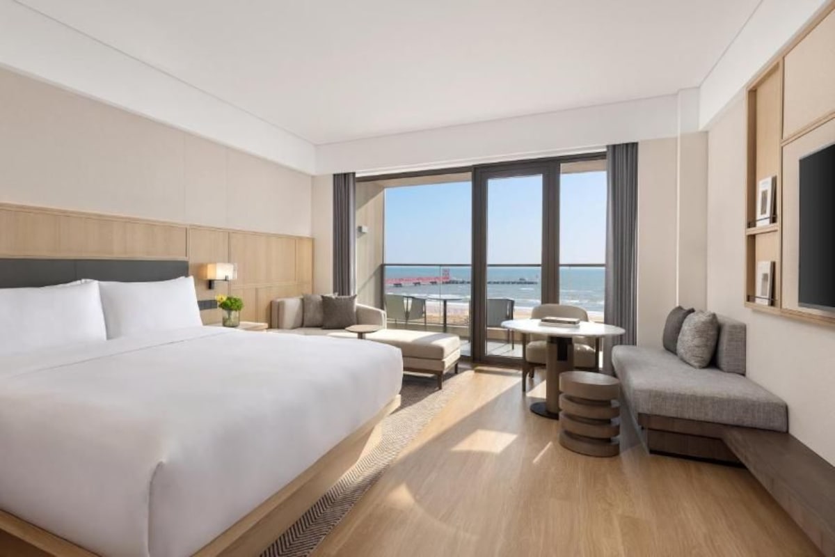 A hotel room with a large bed, a seating area with a table, and a view of the sea.