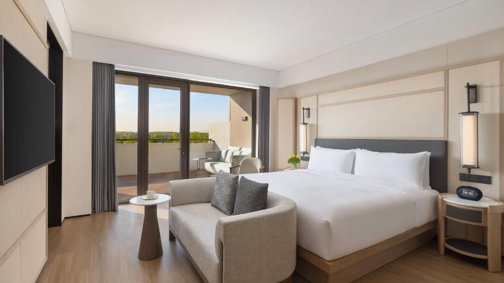 Ein Hotelzimmer mit einem Bett, einer Couch, einem kleinen Tisch, einem Fernseher und einem Balkon mit Sitzgelegenheit.