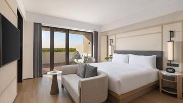 A hotel room with a bed, a sofa, a small table, a TV, and a balcony with outdoor seating.