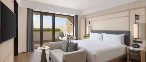 A hotel room with a bed, a sofa, a small table, a TV, and a balcony with outdoor seating.