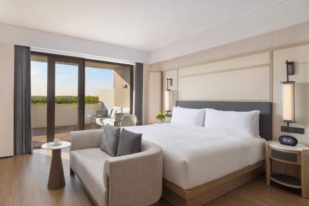 Quarto de hotel com cama, sofá, mesa pequena, televisão e varanda com área de estar.