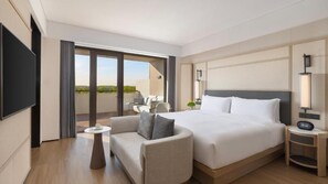 Quarto de hotel com cama, sofá, mesa pequena, televisão e varanda com área de estar.