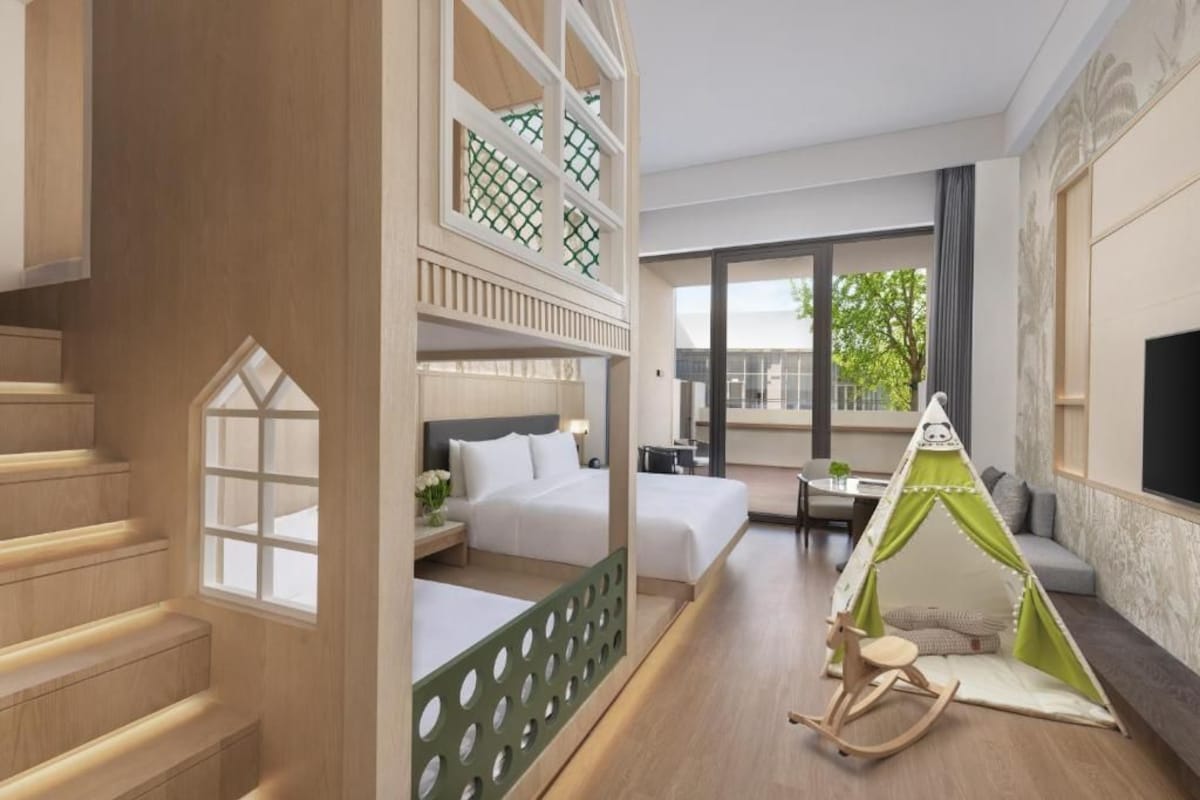 Quarto de hotel com varanda, cama, área de estar e um tenda infantil.