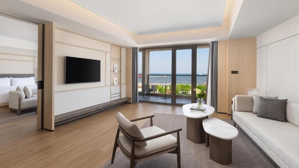A modern hotel room with a balcony, a flat-screen TV, a sofa, a dining table, and a chair.