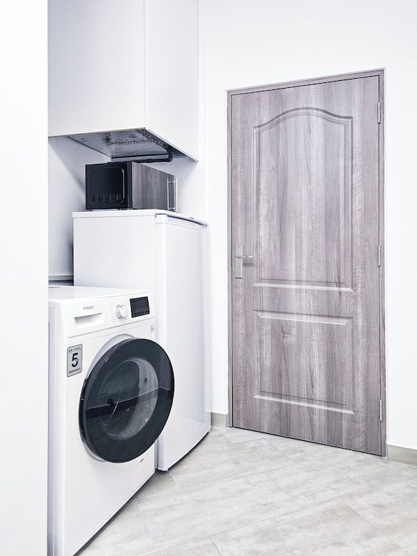 Un área de lavandería compacta con lavadora y secadora, una puerta de madera y piso de baldosas.