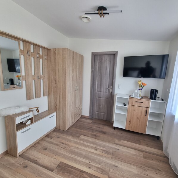 A room with a wooden wardrobe, a white dresser, a TV mounted on the wall, and a door.