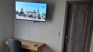 A room with a wooden desk, a chair, a television mounted on the wall displaying a Legoland advertisement, and a door. - Karlskovhuset - Modern & Cozy, 8km from Legoland (Give)
