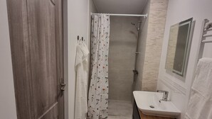 A bathroom with a wooden door, a shower with a floral curtain, a sink with a mirror, and a towel rack. - Karlskovhuset - Modern & Cozy, 8km from Legoland (Give)