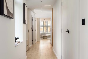 A hallway with white walls, a light wooden floor, and doors leading to a room with a window and a sofa. - 3 Mins Walk to Westminster Abbey, Luxury Retreat (Greater London)