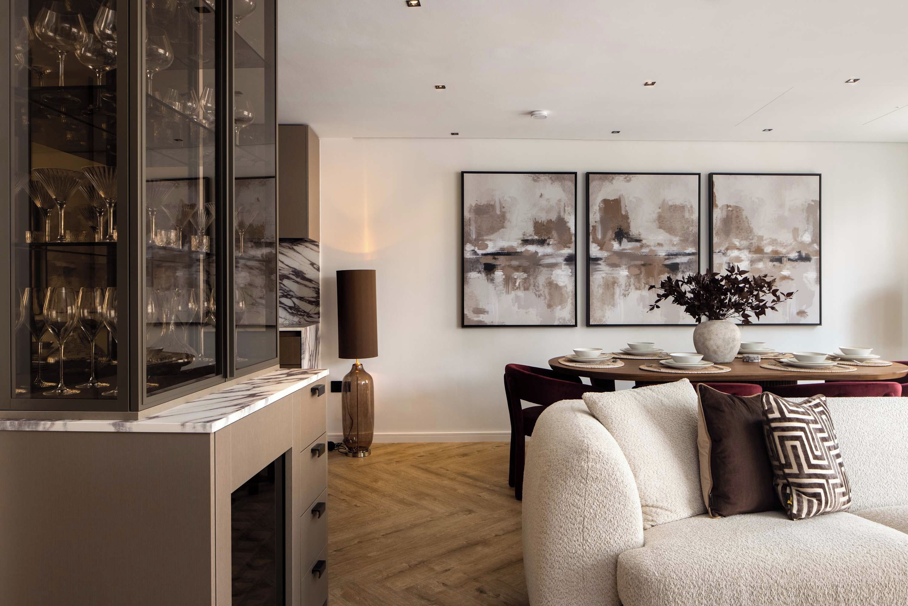 A modern living room with a glass cabinet, a dining table set for four, and abstract paintings on the wall.