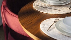 Une table à manger dressée avec de l’assiette blanche, des couverts en argent et un set de table en fibres tressées.