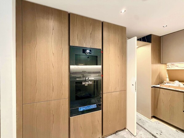 A modern kitchen with wooden cabinetry, a built-in oven, and a countertop. - 5 Mins Walk to Big Ben, Luxury Apartment (Greater London)