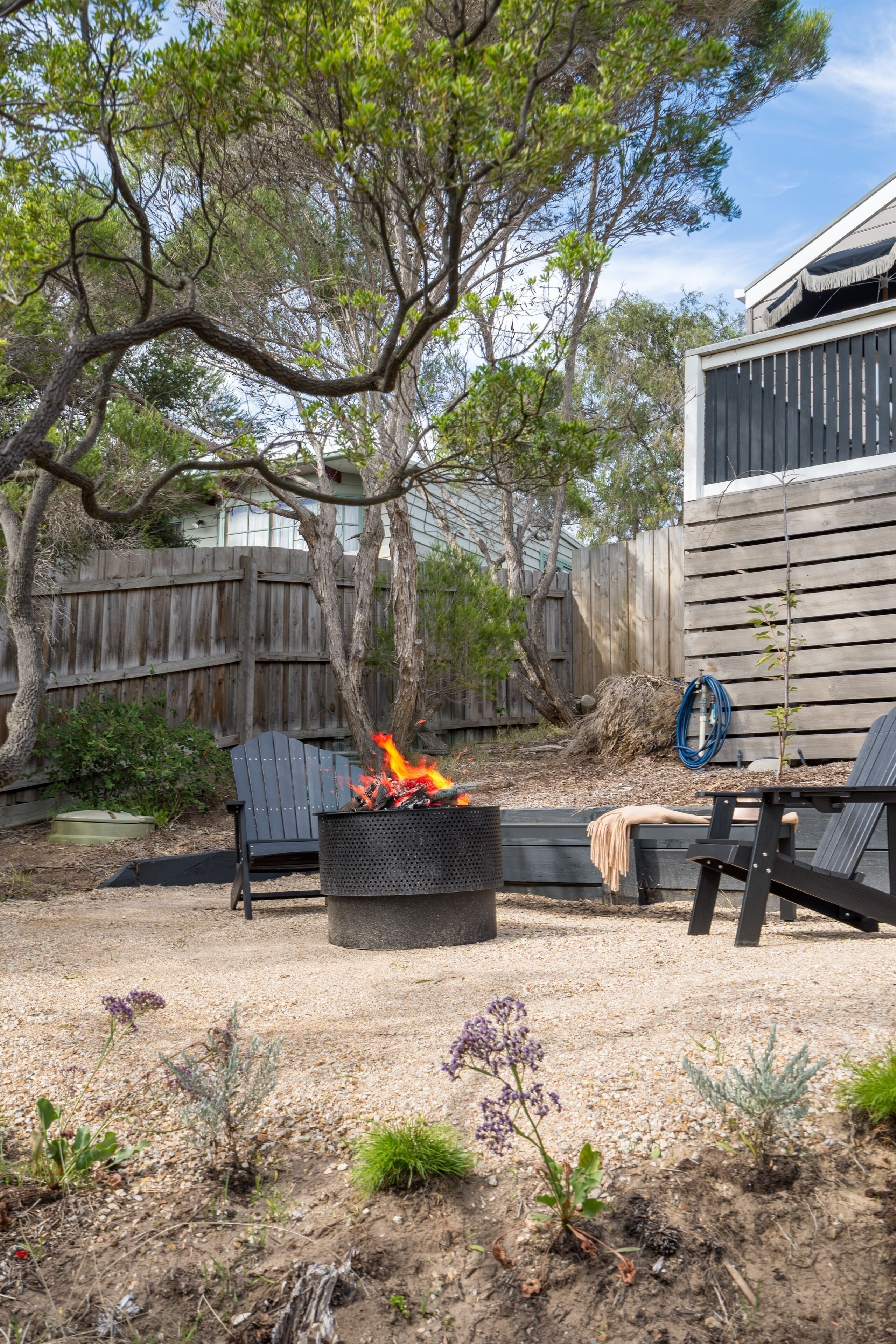 A backyard with a fire pit, two chairs, and a small table.