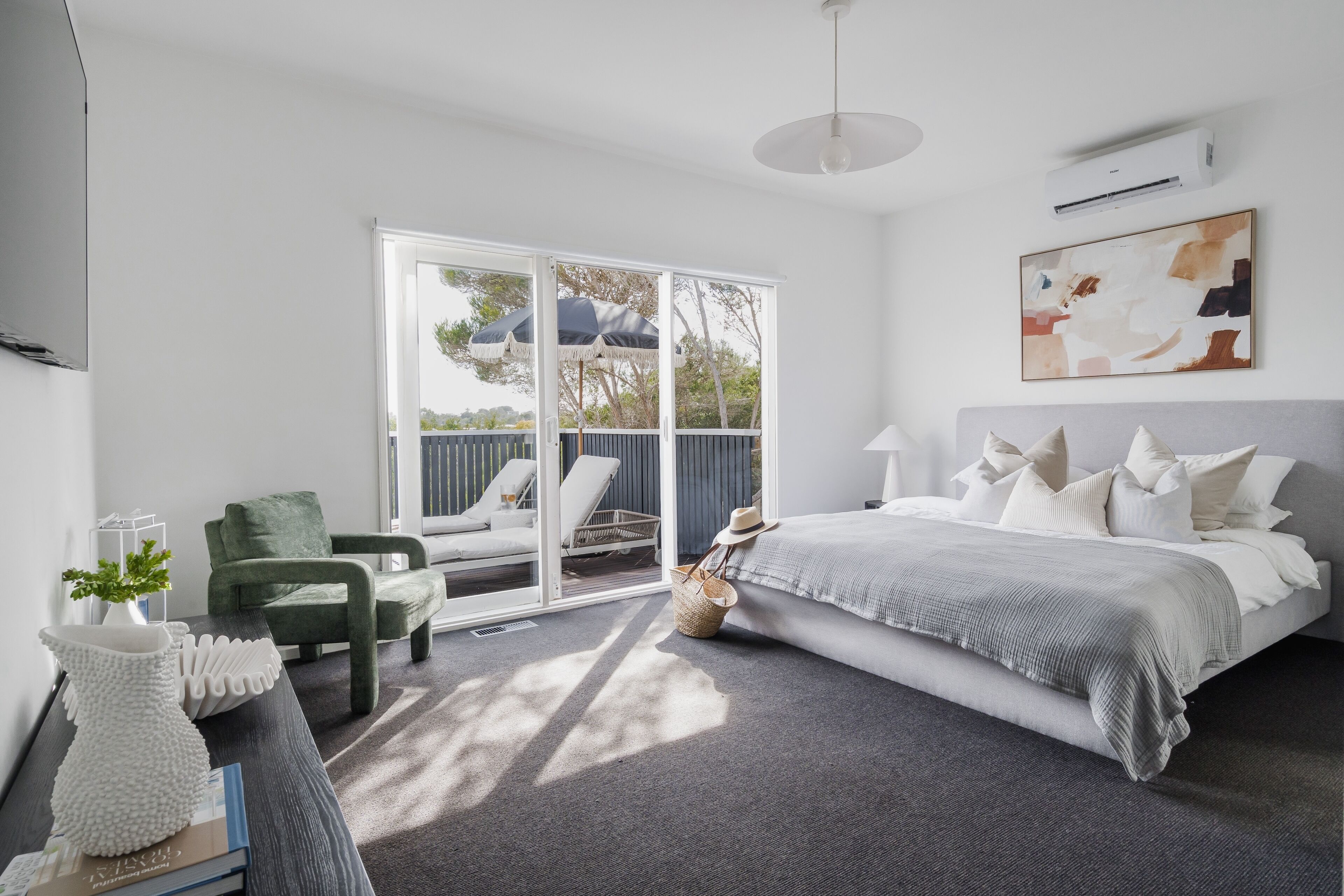 Une chambre à coucher avec un lit, un fauteuil vert, une table de chevet blanche et une grande fenêtre.