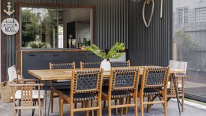Uma sala de jantar com mesa e cadeiras de madeira, um espelho grande e um letreiro indicando uma localização de praia.