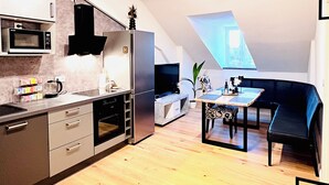 Una cocina moderna con microondas, horno y cafetera, un comedor con mesa y sillas, y un tragaluz.