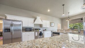 Una cocina moderna con armarios blancos, electrodomésticos de acero inoxidable, encimeras de granito e iluminación colgante.