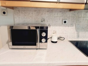 Une cuisine équipée d’un four à micro-ondes en acier inoxydable, d’une bouilloire électrique blanche et d’un dosseret carrelé.