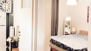 Ett sovrum med en säng, en stol, ett skrivbord, en klocka och en hängande lampa.