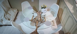 Une pièce avec une table en verre, des chaises blanches, un vase rempli de fleurs et un canapé blanc.