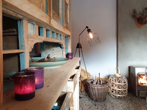 A rustic interior with a wooden shelf, candles, a lantern, a woven basket, and a wood-burning stove. - Charming Garden Holiday Home for 6 (Durbuy)