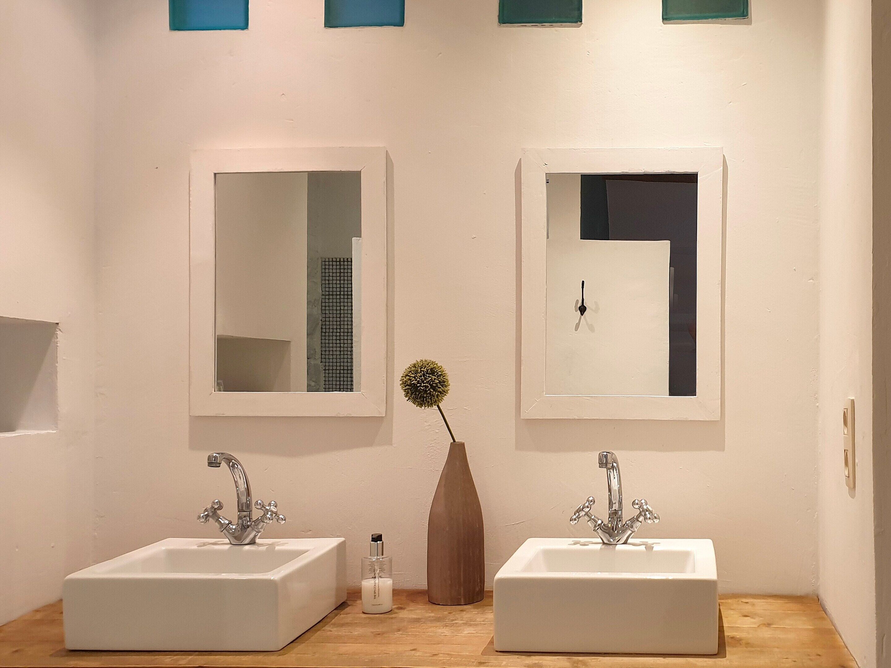 A bathroom with two sinks, a mirror, and a vase with a flower.