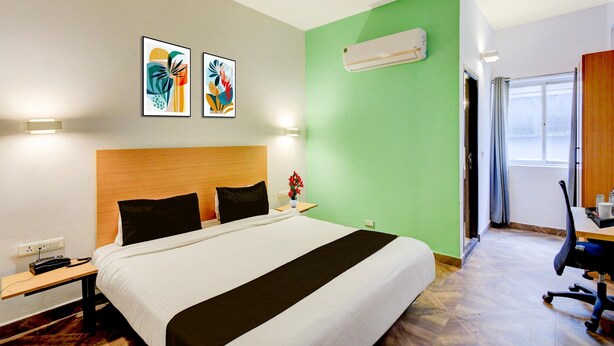 A hotel room with a bed, bedside tables, a desk, and a chair. There are two wall-mounted air conditioners and a window with curtains. - Super Townhouse SR Nagar Metro Hyderabad (Hyderabad)