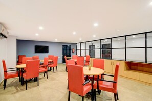 A conference room with red chairs and tables, a flat-screen TV, and a large window with blinds. - Super Townhouse SR Nagar Metro Hyderabad (Hyderabad)