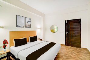 A hotel room with a bed, a bedside table with a vase of flowers, a round mirror, and a wooden door. - Super Townhouse SR Nagar Metro Hyderabad (Hyderabad)