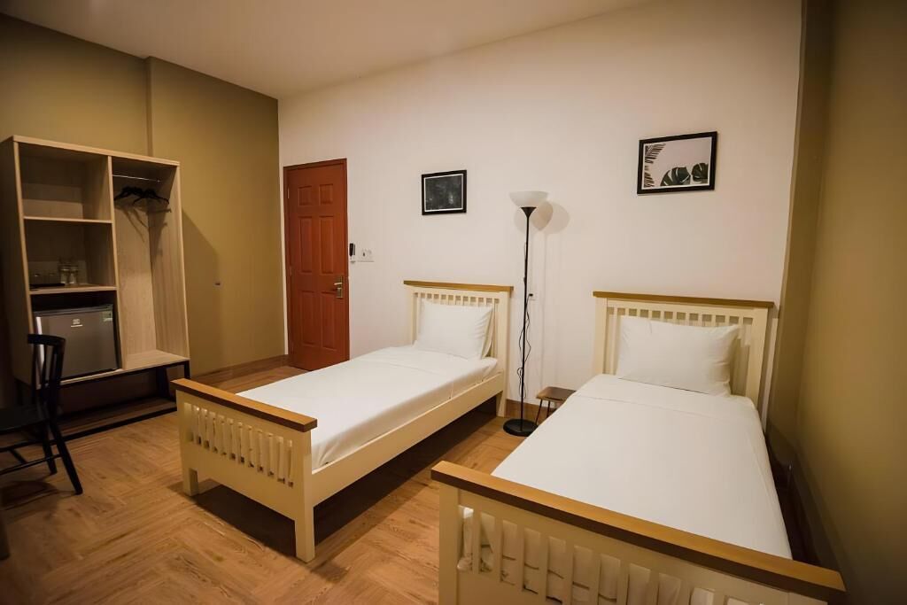 A room with two single beds, a wooden wardrobe, a desk, and a floor lamp.
