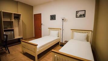 A room with two single beds, a wooden wardrobe, a desk, and a floor lamp.