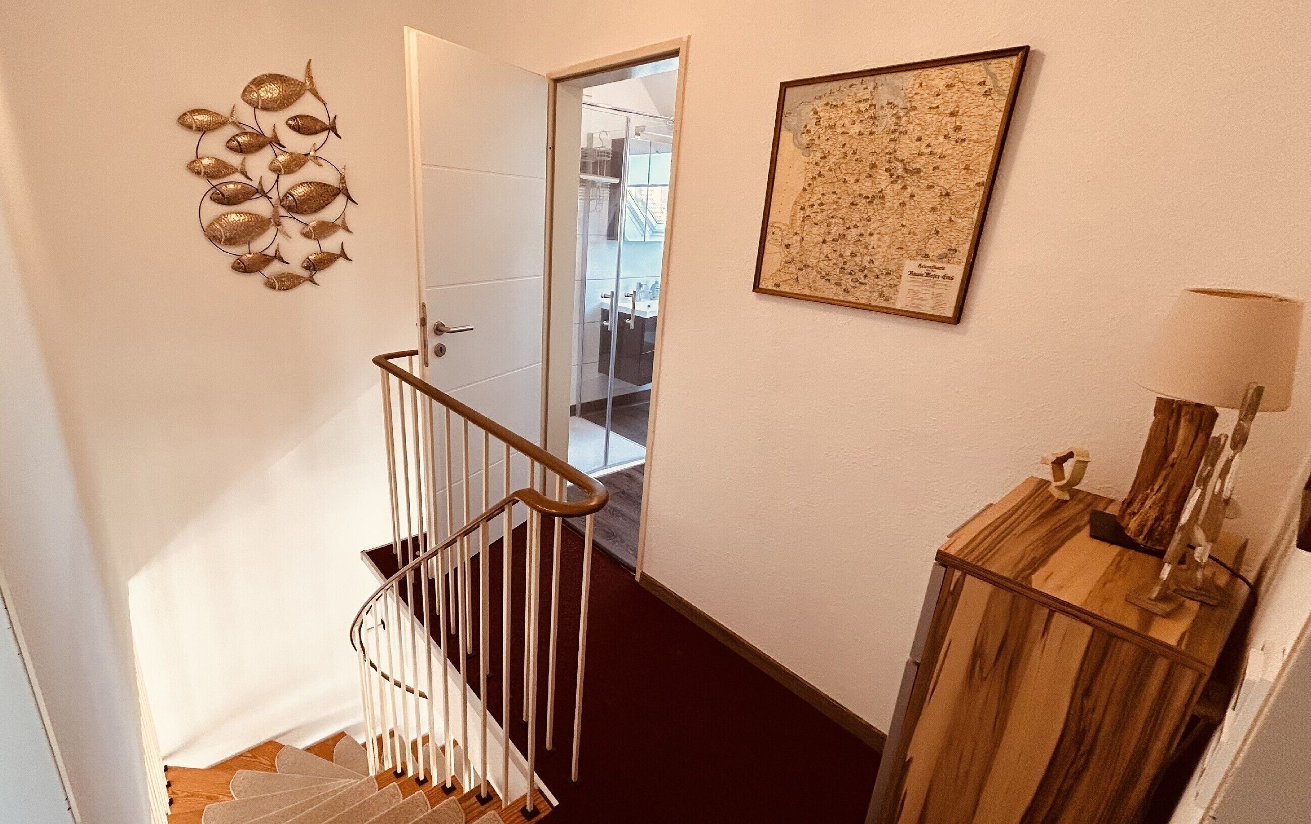 Una escala amb barana blanca, un armari de fusta amb una làmpada i un mapa a la paret.
