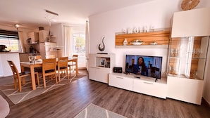 Un saló modern amb zona de menjador, televisió i cuina al fons.