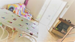 Ein Essbereich mit einem Tisch mit Glasplatte, Stühlen, einer gemusterten Couch und einer weißen Tür im Hintergrund.