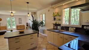 A spacious kitchen with a large island, pendant lighting, and a view of the outdoors. - Villa Oliveraie - Olive Grove Experience (Villecroze)