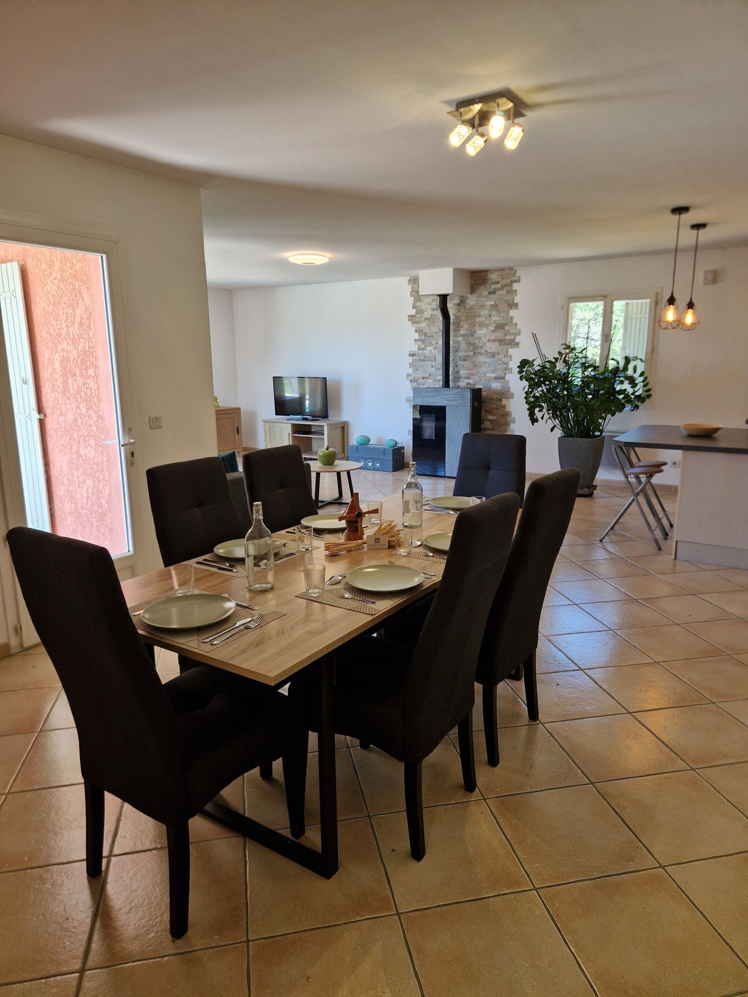 Un coin repas avec une table en bois, des chaises et un téléviseur en arrière-plan.