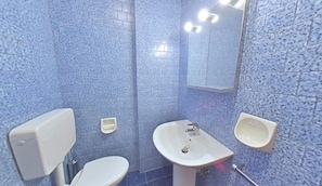 Ein Badezimmer mit Toilette, Waschbecken und Bidet, alles vor einer blauen Fliesenwand.