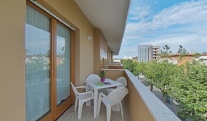 A balcony with a table and chairs, a potted plant, and a view of buildings and greenery. - Lovely Family Stay Near the Beach (Lignano Sabbiadoro)