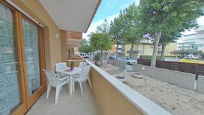 A balcony with a table and chairs, a potted plant, and a view of the street and buildings. - Comfortable Flat With Wifi Near the Town Center (Lignano Sabbiadoro)