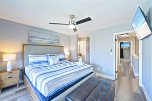 Ein Schlafzimmer mit Bett, Nachttischen, Deckenventilator und einem an der Wand montierten Fernseher.