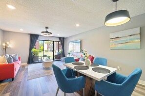 En moderne stue med spiseplads, en rød sofa, blå stole og et stort vindue med udsigt.