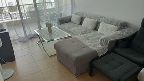A living room with a sofa, ottoman, and glass coffee table. - The Sun Whisper (Chlorakas)