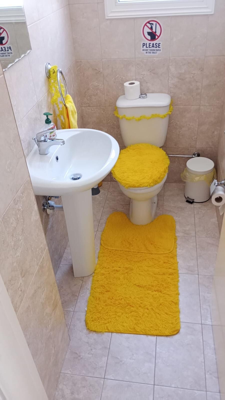 A bathroom with a sink, toilet, and a yellow rug on the floor.
