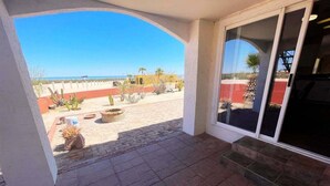Un patio techado con vistas a un paisaje desértico, una puerta corrediza de vidrio y un piso de baldosas de piedra.